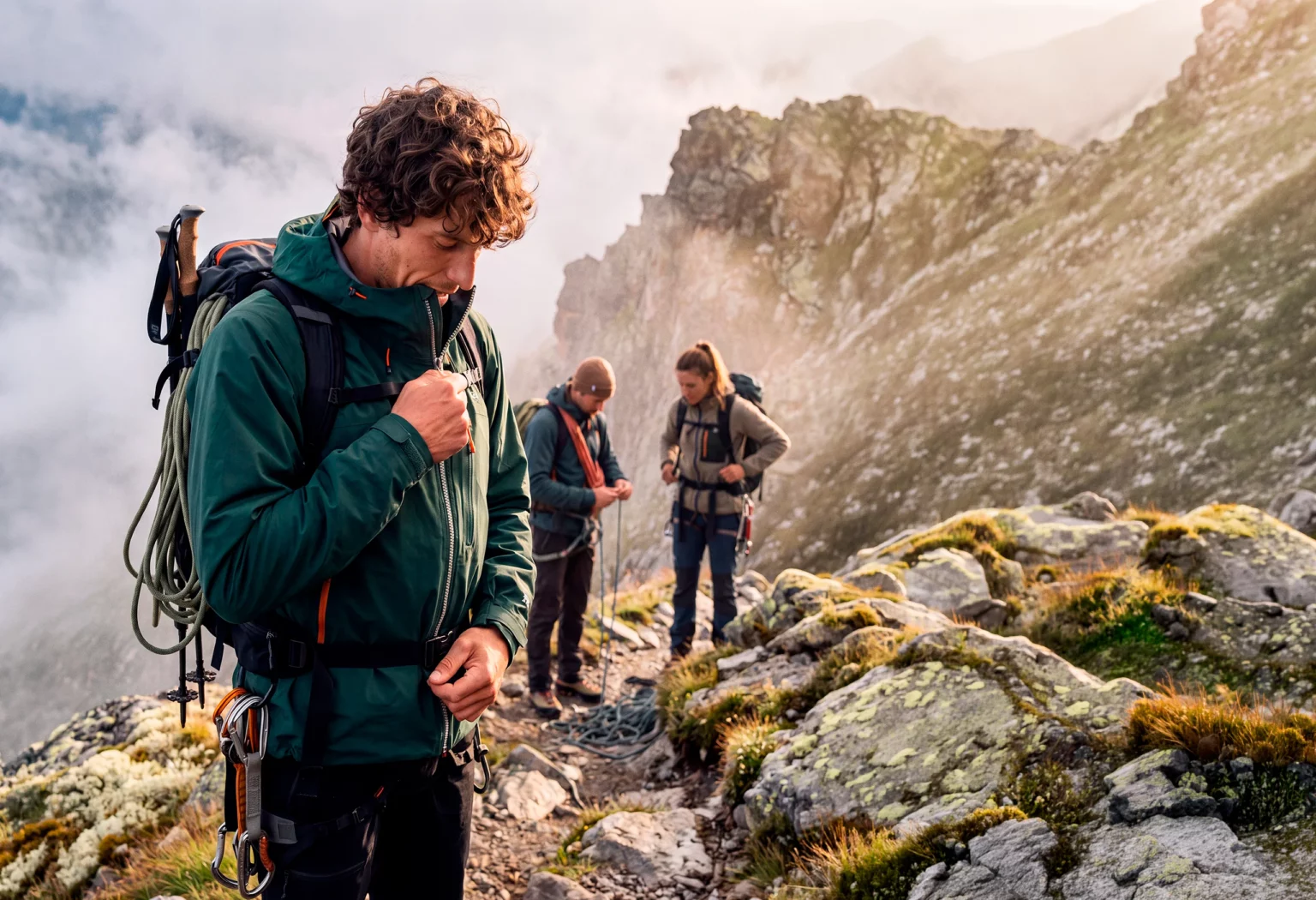Climber closing the zipper of a green jacket on a mountain trail